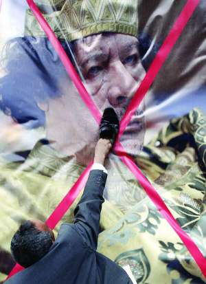 Чоловік біля лівійського посольства у Єгипті б’є черевиком перекреслений портрет Муаммара Каддафі. Сотні людей зібралися 21 лютого в Каїрі на підтримку виступів у Лівії