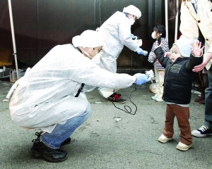 Працівники у захисному одязі за допомогою приладів перевіряють рівень радіації на дітях, яких евакуювали із зони біля атомної електростанції ”Фукусіма Дайні”
