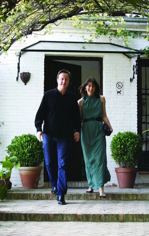 Девід Кемерон разом із дружиною Самантою виходять із готелю в місті Гранада, що на півдні Іспанії. Обоє одягнені по-літньому. На Девіді темно-сині джинси і футболка.  Саманта в зеленому сарафані. На вулиці 23 градуси тепла