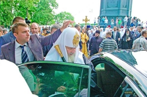 Російський патріарх Кирило сідає у ”мерседес” представницького класу з номерами Верховної Ради після молебню на Володимирській гірці в Києві. Охоронець складає хрест на його головному уборі, аби не зачепився за верх машини