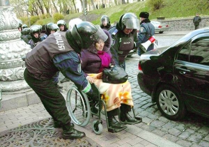 ”Беркутівці” допомагають учасниці акції протесту заїхати інвалідним візком із проїжджої частини на бордюр під Кабінетом Міністрів у Києві. У середу близько 500 чорнобильців протестували проти урізання пенсій