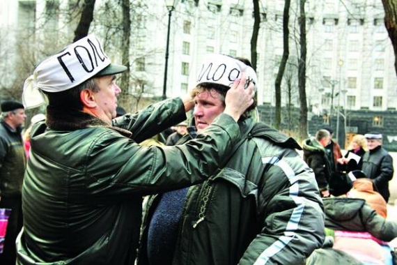 Чоловік чіпляє на шапку іншому пов’язку з написом ”Голодую”. У Маріїнському парку біля Кабінету Міністрів триває акція протесту проти зменшення чорнобильських пенсій. У понеділок зранку до голодувальників долучилася група з Луганщини