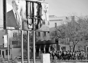 19 грудня 2011 року, місто Жанаозен, Казахстан. Військовий патруль біля плакату президента Казахстану Нурсултана Назарбаєва. На задньому плані видно будівлю, яка горіла під час заворушень 16 грудня. У той день загинули щонайменше 15 осіб