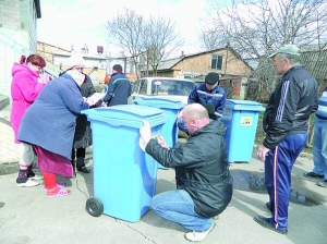 Майстер комунгоспу Анатолій Сух клеїть наклейки на контейнери на Немирівському шосе у Вінниці. На них напис: ”Своєчасна проплата — вчасний вивіз сміття”. Ліворуч Лідія Маслова підписує акт прийому сміттєвого бака