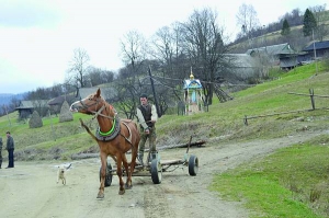 Чоловік їде кіньми центральною вулицею села Межигір’я Турківського району на Львівщині. Позаду — капличка з фігурою Божої Матері. Такі розташовані тут майже на кожному перехресті. Село за 180 кілометрів від обласного центру, тут живуть 288 осіб