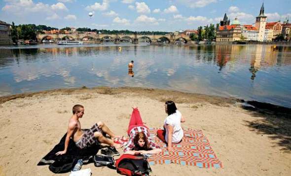 Люди відпочивають на березі річки Влтави у чеській столиці Празі неподалік Карлового моста, одного з найдавніших у країні. За ним видно Празький град - історичну частину міста