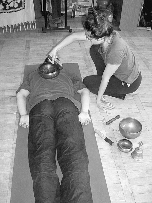 Інструктор зі звукового масажу Ірина Школьник водить дерев’яною паличкою по тибетській чаші на спині вінничанина Валентина Чернишова. Звук вібраціями розходиться по тілу