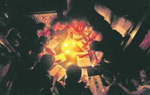 Учителька показує ручкою рядки у зошиті, які має прочитати школярка. Учні сидять тісним кільцем навколо свічок посеред класу в індійському місті Калькутта, 31 липня