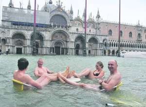 У неділю люди сидять за столом на площі Сан-Марко у Венеції. Через сильні дощі туристи ходять по місту в гумових чоботях, дехто плаває