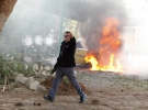 Израильский полицейский бежит на фоне автомобиля, который загорелся вследствие попадания палестинской ракеты