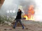 Ізраїльський поліцейський біжить на фоні автомобіля, що загорівся унаслідок попадання палестинської ракети