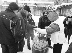  Безхатьків годують гречаною кашею, кабачковою ікрою і хлібом на столичному залізничному вокзалі. Жінка у фартуху розкидає їжу по пластикових тарілках