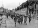 Командир 1-ї роти 314-го піхотного полку 79-ї піхотної дивізії армії США капітан У. Хупер (WH Hooper) (буде убитий на початку липні в боях за Ля Е-дю-Пюї (La Haye-du-Puits)) зі своїми людьми конвоює полонених німецьких солдатів вулицею французького міста Шербур