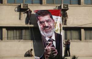 Прихильники усунутого від влади єгипетського президента Мухаммеда Мурсі вішають його портрет на будівлі навпроти штаб-квартири Республіканської гвардії в столиці Каїр, де, як вони думають, утримують під вартою їхнього лідера. У понеділок уранці дехто з мітингувальників спробував штурмувати військовий об’єкт. У відповідь солдати відкрили вогонь