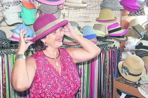 Ніна Набокіна приміряє червоний капелюшок із целюлози у магазині ”Черевички” в Черкасах. Продавець каже, що цього року почали купувати головні убори для міста, а не для пляжу