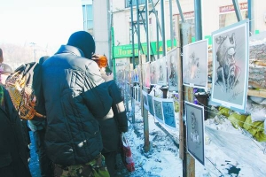 Люди розглядають виставку карикатур. Її розмістили на огорожі біля готелю ”Дніпро”. Плакати та малюнки зробили майданівці у Вільному університеті, розташованому в Українському домі