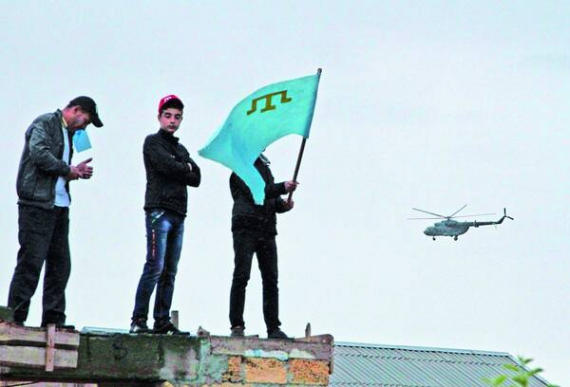 Чоловіки тримають кримськотатарські прапори під час мітингу в пам’ять про масові депортації з регіону 18 травня в Сімферополі. Довкола постійно кружляє військовий вертоліт