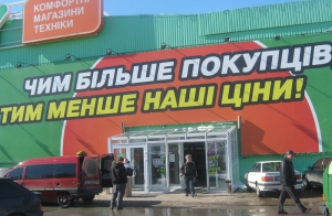 Вислів "тим менше наші ціни" - недоперекладений із російської. В українській за ним проситься ще якесь дієслово. Наприклад, "тим менше наші ціни кусаються". А те, що мали на думці рекламісти, правильно так: "тим менші наші ціни". Такою каламбурною була реклама мережі Comfy в різних містах України. Фото - blitz.if.ua