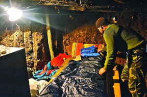 Боєць 19-го батальйону територіальної оборони Миколаївської області застилає саморобне ліжко у бліндажі. Одяг, спорядження бійцям привозять волонтери. Також солдати купують за власні гроші