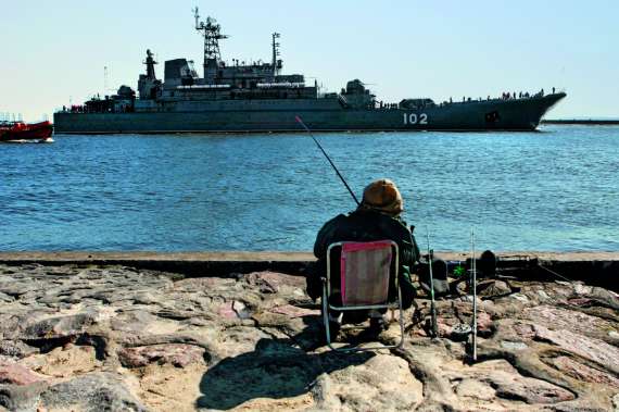 Калінінградський рибалка сидить на березі біля десантного корабля, який пригнали в док з нагоди урочистостей 9 Травня