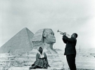 28 січня 1961-го американський джазовий музикант 60-річний Луї Армстронґ грає на трубі біля єгипетських пірамід. Поряд сидить четверта й остання його дружина – танцівниця, яку він називав ”Мама Люсіль”. За два роки до цього музикант пережив інфаркт. Фото зроблене  під час благодійного туру, в рамках якого Армстронґ дав безкоштовні концерти в 27 містах