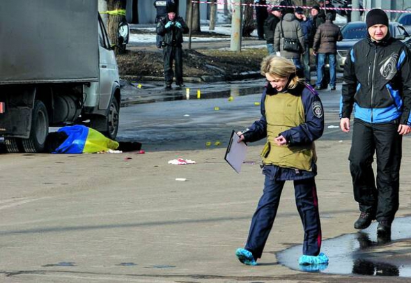Міліціонер оглядає місце вибуху саморобного пристрою 22 лютого на проспекті Маршала Жукова в Харкові. Біля ”Газелі” лежить накритий синьо-жовтим прапором загиблий чоловік. Всього постраждали 13 людей