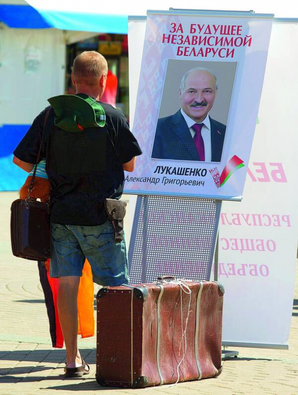 Чоловік стоїть поруч із портретом президента й кандидата в президенти Білорусі Олександра Лукашенка. 11 жовтня вп'яте переобрали його на цей пост. На вибори Лукашенко йшов із гаслом ”За майбутнє незалежної Білорусі”