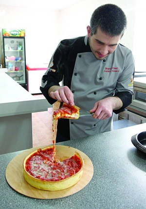 27-річний шеф-кухар Аслан Абаєв розрізає піцу-пиріг. Між шарами тіста начинка: смажена курка, ковбаса пепероні та сир моцарела