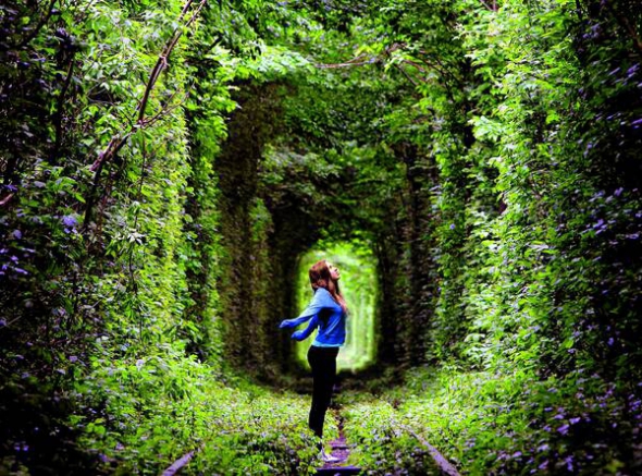 Дівчина стоїть у Тунелі кохання біля селища Клевань Рівненського району. Це ботанічний феномен із заростей дерев і кущів, які сплелися й утворили щільний коридор точної арочної форми. Тунелем проходить залізнична колія