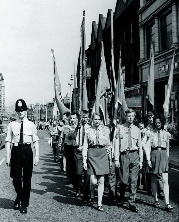 Демонстрація Спілки української молоді в Олдгемі, Велика Британія, 1970-ті. Колону – з прапорами синьо-жовтими та спілки – супроводжує поліція