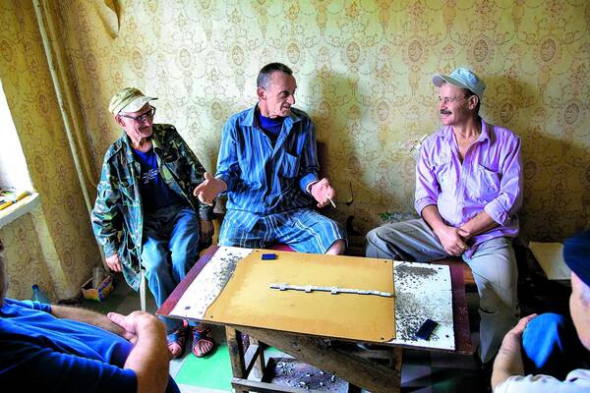67-річний Петро Завалко, 68-річний Олександр Кубишин і 56-річний Андрій Опаренко грають в доміно у одній з кімнат 3-кімнатної квартири їхнього друга, який живе у Липняжці