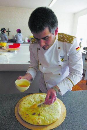Шеф-кухар Аслан Абаєв змащує готовий осетинський пиріг кухарським пензликом, змоченим у розтопленому маслі  