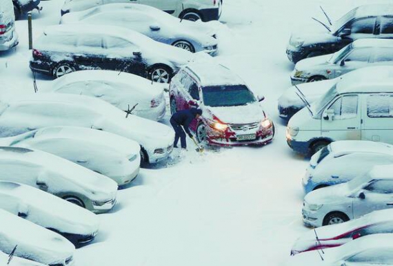 Чоловік відкидає сніг із дороги на парковці в Києві. Снігопад у столиці почався зранку 13 листопада. Через це в місті утворилися великі затори, погано ходив транспорт