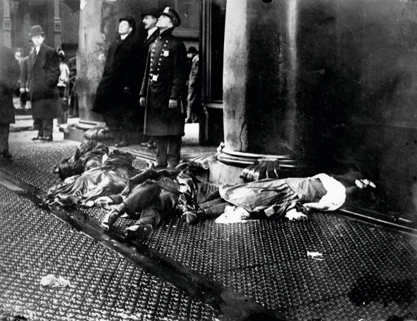 Перехожі та поліцейський спостерігають за пожежею на фабриці одягу Triangle Waist Company в Нью-Йорку 25 березня 1911 року. На тротуарі лежать тіла працівниць, які вистрибнули з вікон восьмого-десятого поверхів