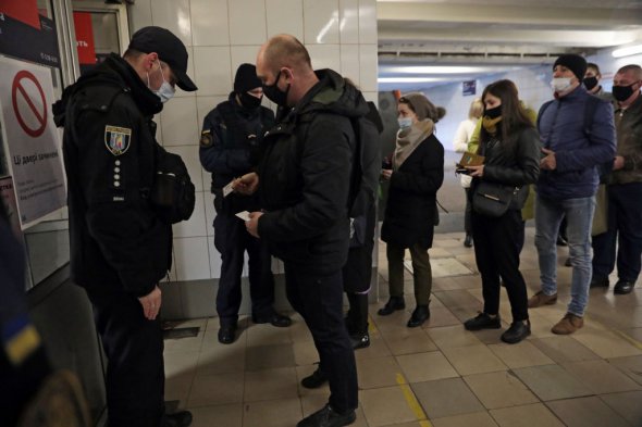 Мужчина показывает специальный пропуск для проезда полицейскому на входе в одной из станций метро.