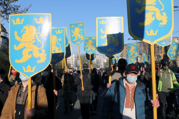 Участники марша несут таблички с изображением золотого льва на голубом фоне - символа дивизии СС "Галичина"