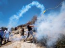 Палестинский демонстрант отбрасывает баллончик со слезоточивым газом, выпущенный израильскими войсками во время акции протеста против израильских поселений в Бейте на оккупированном Израилем Западном берегу