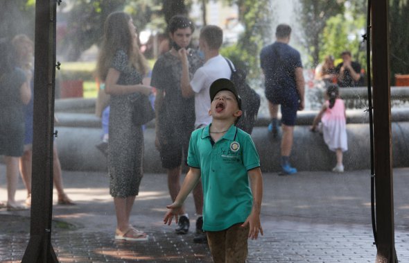 Дети купаются под рамками-увлажнителями в Киеве 16 июля. В течение недели в столице держалась жара, столбики термометров поднимались выше 37С