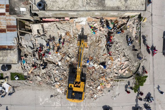 Люди ищут свои вещи, пока экскаватор вывозит щебень из разрушенного здания после землетрясения магнитудой 7,2 балла.