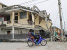 Люди проезжают на мотоцикле мимо поврежденного дома после землетрясения магнитудой 7,2 балла.
