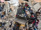 Люди шукають свої речі, поки екскаватор вивозить щебінь зі зруйнованої будівлі після землетрусу магнітудою 7,2 бала.