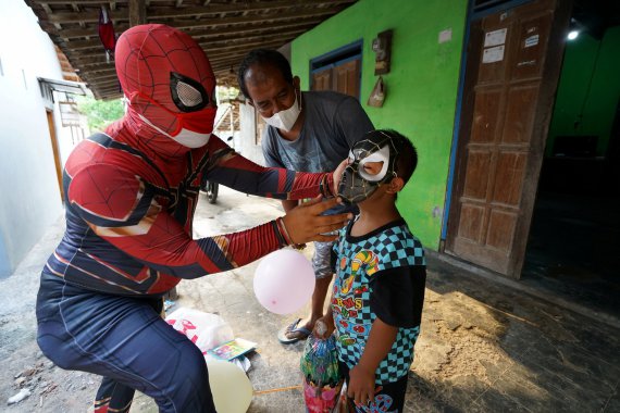 40-летний мужчина в костюме супергероя развлекает мальчика, мать которого умерла от коронавирусной болезни (COVID-19), в маске Человека-паука в Сукохарджо, провинция Центральная Ява, Индонезия