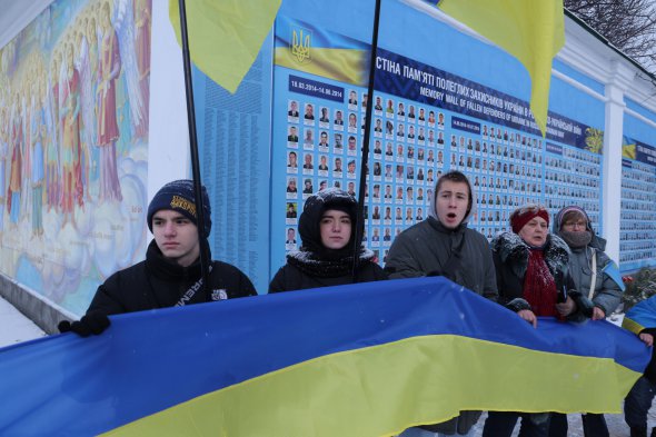 Украинский флаг в руках молодых парней на фоне стелы с именами погибших в российско-украинской войне в День злуки, Киев, 22 января