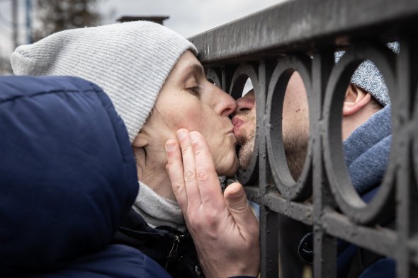 Олег цілує на прощання дружину Яну через паркан залізничної платформи, поки вона чекає на посадку в евакуаційний потяг з їх 11-місячним сином після втечі від запеклих боїв у Бучі та Ірпені, 4 березня 