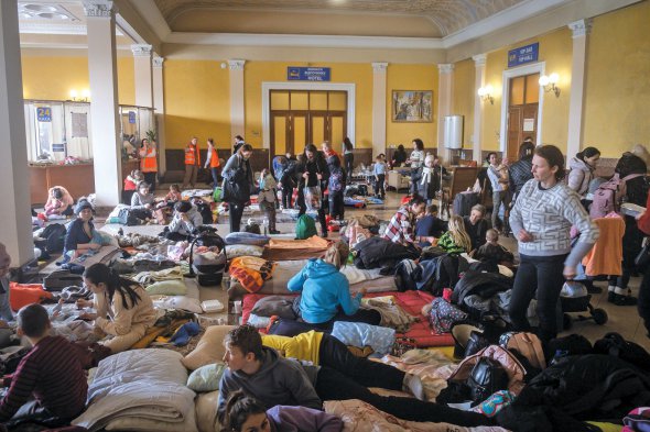 Люди чекають на прибуття евакуаційних поїздів у залі очікування Львівського вокзалу. Щодоби тут проходять 20 міжнародних рейсів. Найчастіше поїзди їдуть до Перемишля і Хелма в Польщі. Щодня через Львівський вокзал проходить у середньому 30–40 тисяч людей. — Такої кількості пасажирів наш вокзал ще не бачив. Але в біді ми не залишимо нікого, — говорить мер Львова 53-річний Андрій Садовий. — Десятки організацій і сотні волонтерів роблять усе можливе для забезпечення комфорту і порядку на вокзалі.