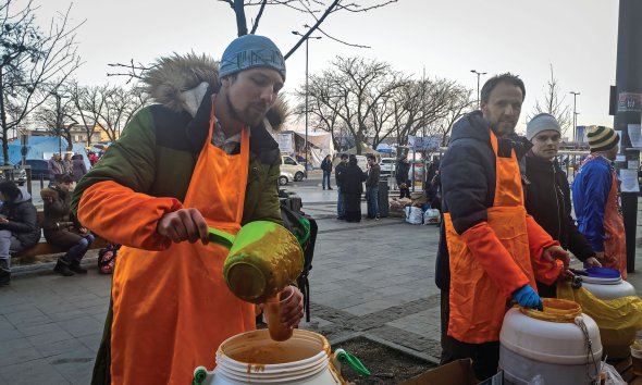 Біля Львівського вокзалу волонтери розливають для біженців у пластикові стакани овочеву зупу. Готують її з бобів, картоплі й томатів