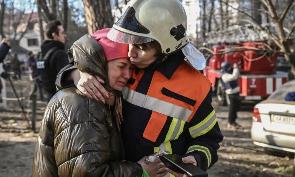 Рятувальники втішають евакуйованого жителя біля будинку, що горить у Києві 