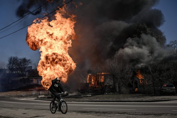 Велосипедист проїжджає повз полум'я та дим, що піднімається від пожежі після артилерійського вогню на 30-й день вторгнення російських військ в Україну на північному сході Харкова, 25 березня 2022 року. - Російський удар по медичній установі в Харкові 25 березня 2022 року вбив щонайменше чотирьох мирних жителів і ще кількох поранив, повідомили українські чиновники.