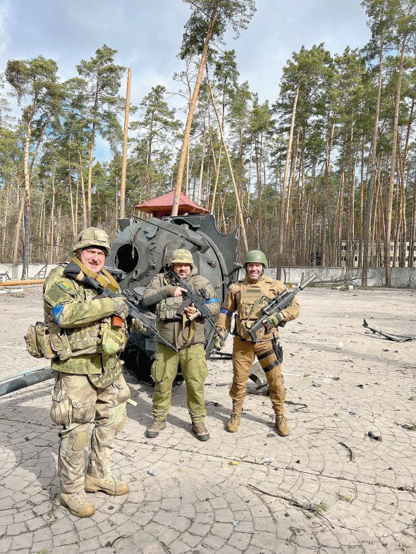 Українські воїни позують біля обгорілих уламків російської техніки в Ірпені. 28 березня місто повністю звільнили від окупантів
