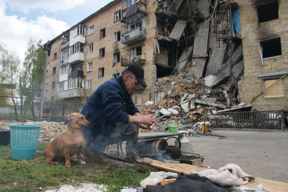 Чоловік гріє воду на вогнищі в Гостомелі на Київщині. Селище 42 дні було окуповане. Багато будинків зруйновані. Тривають роботи по відновленню газо-, електропостачання, подачі питної води.